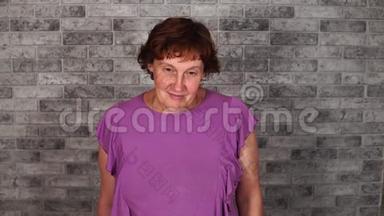 一个漂亮的成熟女人穿着休闲服，短发微笑着，在灰色的砖块背景上看着相机。
